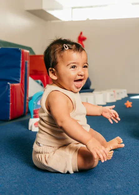 A smiling baby sitting on the floor of the Dynamic Solutions gym