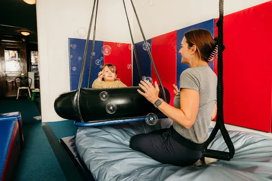A therapist helping a child on a swing in the Dynamic Solutions gym