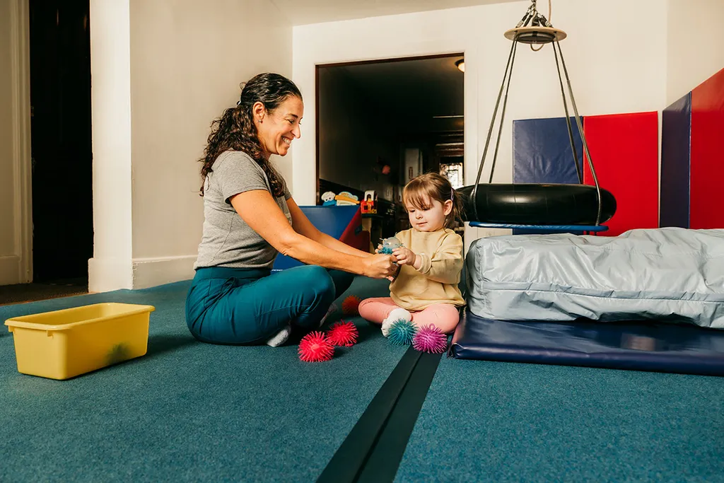 A therapist and a toddler playing together on the floor of the Dynamic Solutions gym